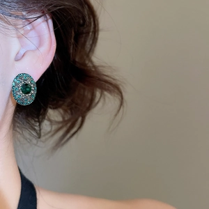 Close-up of vintage oval stud earrings with green rhinestones worn by a model