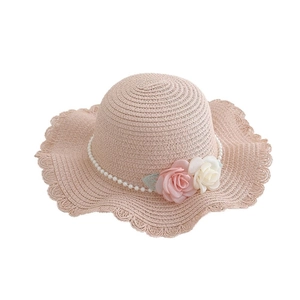 Pink straw sun hat with wavy brim, featuring decorative roses and pearl string embellishments