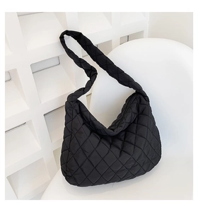 Detail of a black quilted nylon tote bag resting on a white chair in a bright studio