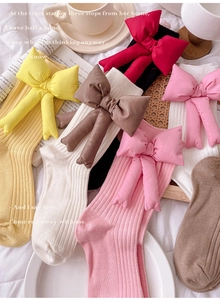 Flat lay of colorful ribbed mid-calf socks with detachable oversized bows on soft bedding