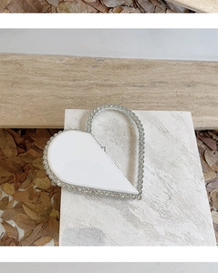 Detail of white heart-shaped evening clutch with sparkling rhinestone handle and edges
