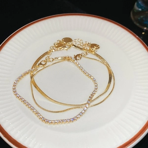 Detail of gold tennis bracelet and flat snake chain on a white ceramic plate