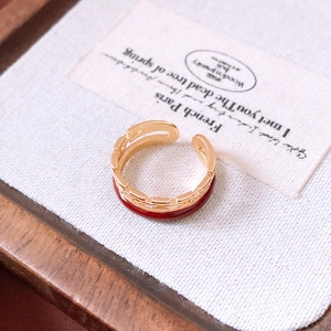 Detail of gold plated double-layer chain ring with dark red enamel on white linen fabric