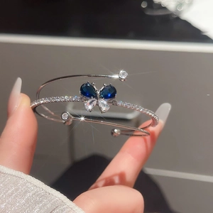 Dettaglio di bracciale rigido a farfalla con zirconi a goccia blu e bianchi