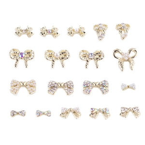 Lot de 17 breloques de nœuds dorés pour ongles avec perles et strass sur fond blanc