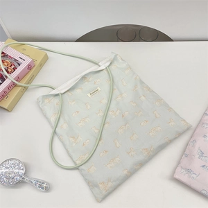 Detail of blue canvas tote bag with orange cat print and green cord strap on white table