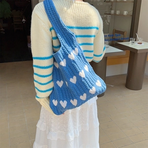 Detail of blue knitted tote bag with white heart patterns in a casual cafe setting