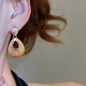 Close-up of golden teardrop hollow earrings with elegant striped texture on ear