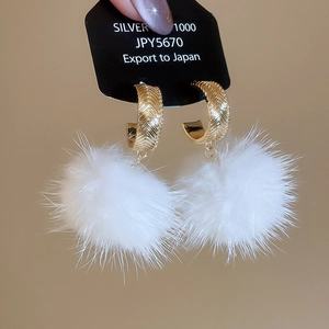 Detail of silver 1000 earrings featuring a white fluffy pom-pom and golden C-ring buckle