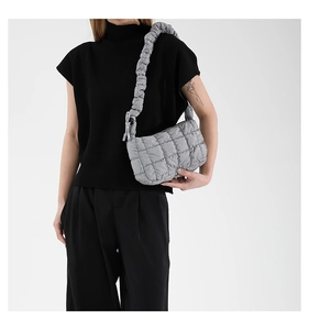 Detail of grey quilted shoulder bag featuring wide ruched cloud strap on model