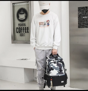 Street style shot of a casual man carrying a large capacity camouflage backpack in white sweatshirt