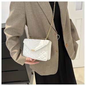 Détail d'un sac bandoulière blanc matelassé avec chaîne dorée porté par un mannequin