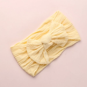 Macro detail of pale yellow knitted baby headband featuring a large bow and cable texture