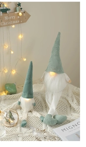 Luminous mint green faceless Christmas gnomes on white knit blanket with warm lights
