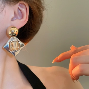 Détail d'une boucle d'oreille géométrique en losange avec perles dorées et zircon