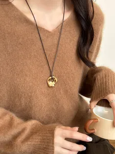Irregular gold hollow pendant with brown cord styled on a sweater for daily wear