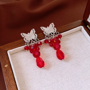 Detail of silver butterfly earrings with red crystal bead tassels on a white velvet tray
