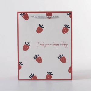 Detail of cream paper gift bag with red border, strawberry patterns and holiday text