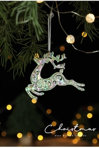Iridescent acrylic reindeer pendant hanging on a green pine branch with bokeh background