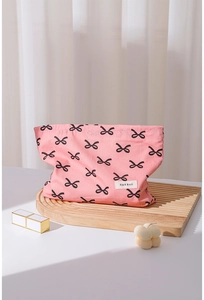 Detailed close-up of a pink cotton makeup bag with black bow patterns on a wooden tray
