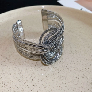 Macro shot of silver woven metal wire knot detail on minimalist open cuff bracelet