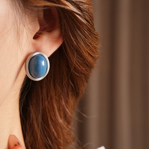 Close-up of vintage blue enamel oval stud earrings worn by a model with blurred hair