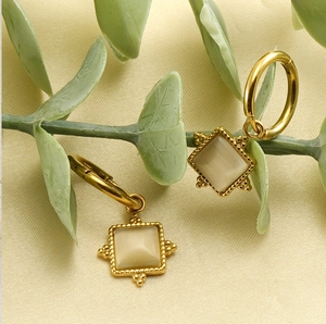Close-up of golden square cat eye stone earrings displayed on textured beige cloth