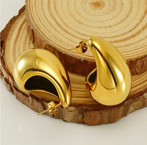 Detailed view of chunky 18K gold teardrop earrings displayed on natural wooden slices