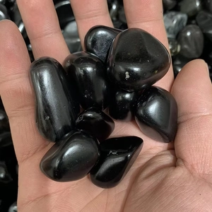 Polished black obsidian tumbled stones in palm for garden and aquarium decoration
