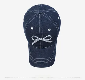 Detailed top view of navy denim baseball cap with white bow embroidery and stitching