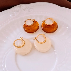 Close-up of 18k gold-plated resin hoop earrings in amber tortoise and ivory white cream