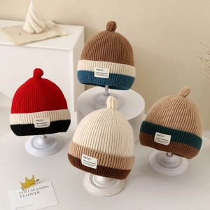 Detail of color-block striped knit baby hats with pom-poms and Hello fabric labels