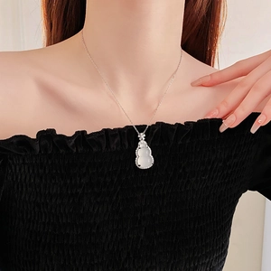 Detail of a silver gourd pendant necklace with white gemstone and zircons on a model