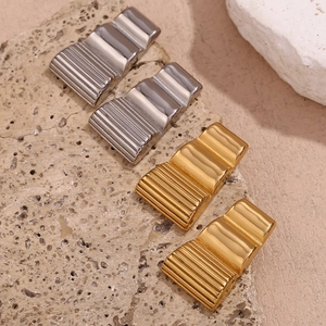 Macro shot of gold and silver wavy trapezoid studs on a natural stone surface