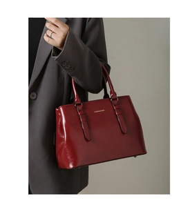 Detail of burgundy glossy leather handbag with gold embossing and decorative straps