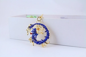 Macro detail of golden dragon keychain with blue enamel and pearl accent on a white box