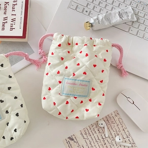 Flat lay of a beige heart quilted drawstring pouch on a minimalist white desk