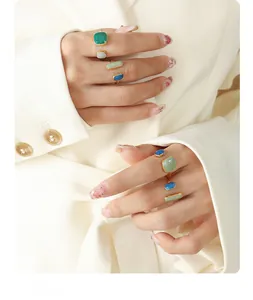 Close-up of stacked gold adjustable rings with colorful enamel on a model in white suit