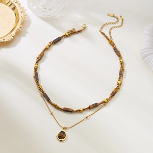 Detail of layered gold necklace featuring tiger eye stone beads and a round pendant