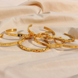 Detailed close-up of gold-plated bangles with star and zircon inlay on silk background