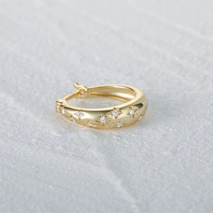 Detailed macro view of a gold huggie hoop earring with starburst pattern and small gems