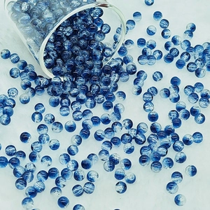 Detailed view of 6mm blue and white marble pattern glass beads pouring onto white fabric