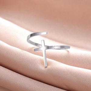 Detail of silver cross open ring on pink silk fabric showing polished metal finish