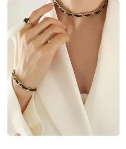 Détail du collier en chaîne dorée et cuir noir avec une bague ornée d'une gemme