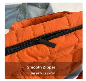 Close-up of a smooth black zipper and diamond quilting on a bright orange tote bag