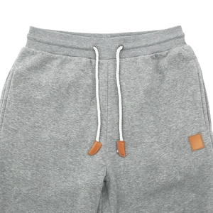 Detail of grey jogger waistband featuring white woven drawstrings and brown leather patch