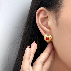 Close-up of red heart earrings with golden radial texture worn on ear for elegant style