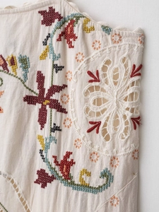 Detailed close-up of colorful embroidery and hollow lace on a cream cotton dress