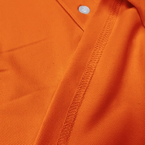 Macro detail of orange pique polo shirt showing high-quality stitching and white button