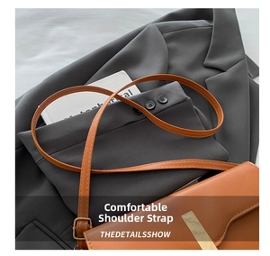 Detailed view of brown leather saddle bag with gold buckle on grey suit background